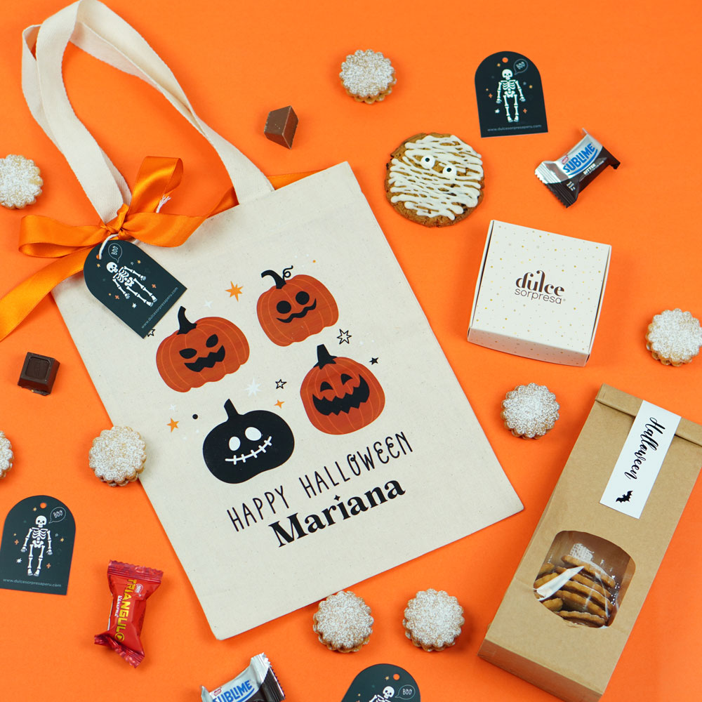 Dulce Halloween: bolsa de tela con calabazas, galletas, chocolates, cajitas y etiquetas de esqueleto sobre fondo naranja